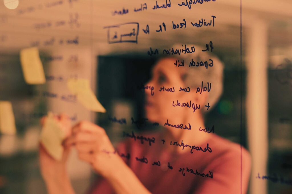 Woman standing in front of pane of glass with brainstorming notes written on it on marker pen, along with post-it notes in strategic planning process.
